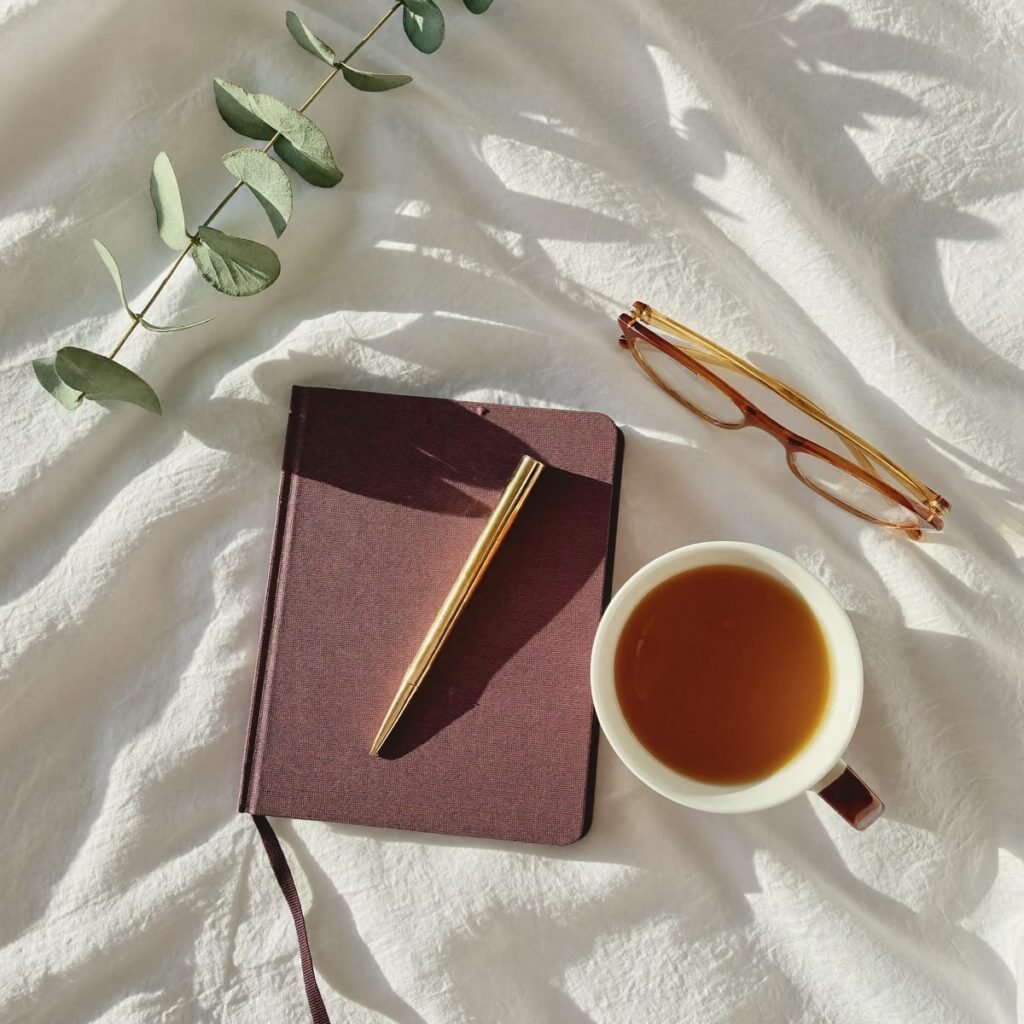 Cuaderno de tapa dura color vino con una pluma dorada y una taza de té